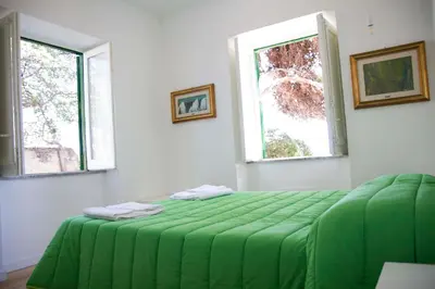a green bed in a white room with two windows at Villa Mallandrino in Mondello