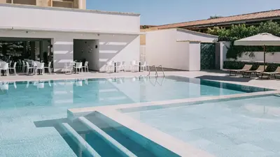 a swimming pool with chairs and tables and a building at Mangia's Himera Resort in Campofelice di Roccella