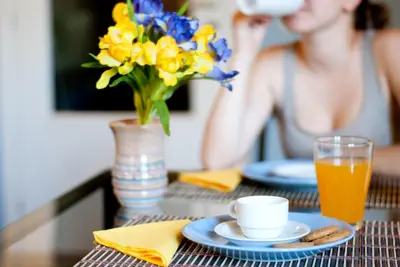 a woman sitting at a table with a vase of flowers and juice at Affittacamere B&B Carella in Palermo