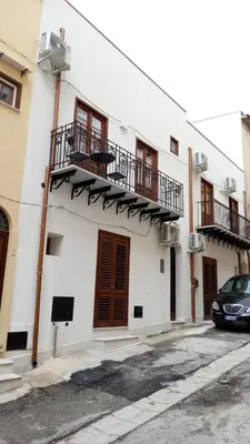 a white building with balconies and a car parked in front at Casa Leonardo e Romeo in Castellammare del Golfo