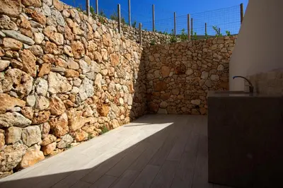 a stone wall with a wooden floor in front of it at Villa Vitruvio - Giardino degli Allori Scopello in Castellammare del Golfo