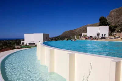 a pool with blue water and buildings in the background at Villa Vitruvio - Giardino degli Allori Scopello in Castellammare del Golfo