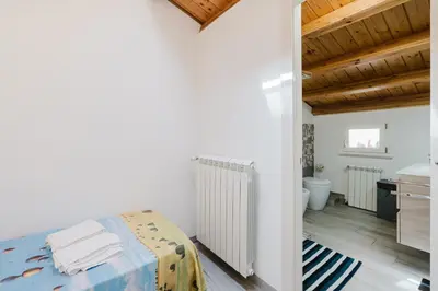 a white bedroom with a bed and a bathroom at Costa del Golfo in Castellammare del Golfo