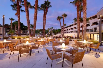 an outdoor patio with tables and chairs and palm trees at The Signature Level at Grand Palladium Sicilia Resort & Spa in Campofelice di Roccella