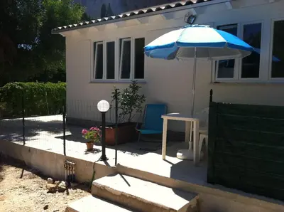 a house with a blue umbrella and a table and chair at Casa Vacanze Mari in San Vito lo Capo