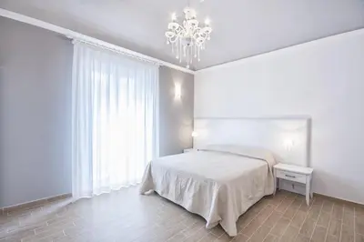 a white bedroom with a bed and a chandelier at Residenza Le Zagare in Castellammare del Golfo