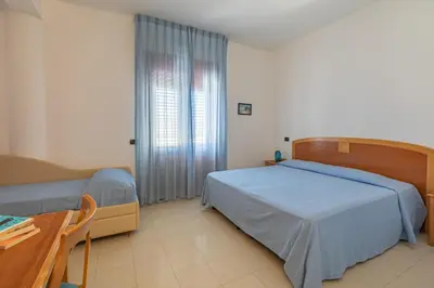 a bedroom with two beds and a table and a window at Hotel Sabbia d'Oro in San Vito lo Capo