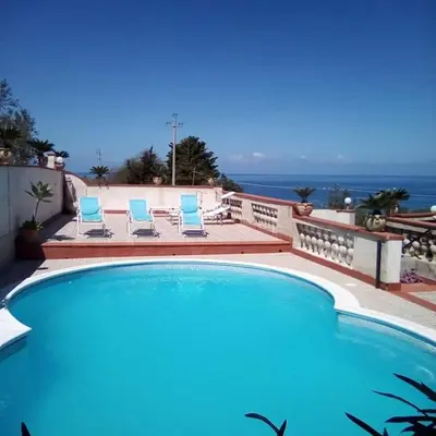 a swimming pool with two blue chairs and the ocean at Villa Teresa in Trappeto