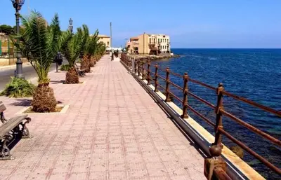 a sidewalk next to the ocean with palm trees at Casa Olivella in Santa Flavia
