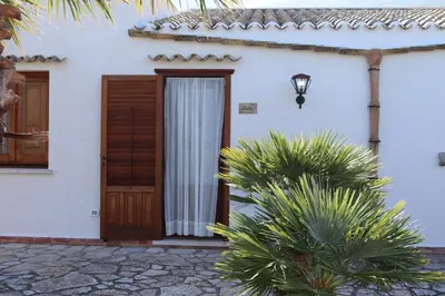 a white house with a wooden door and some plants at Baglio Cracchiolo Casa Baldo in San Vito lo Capo