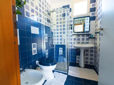 a blue tiled bathroom with a toilet and a sink at Villa Claudia in Scopello