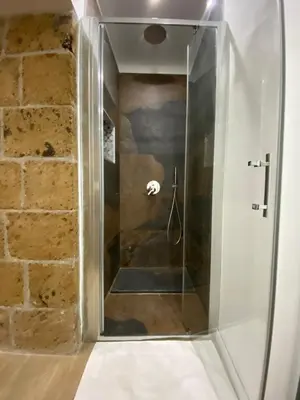 a glass shower in a bathroom with a brick wall at Antico vicolo di ballarò in Palermo