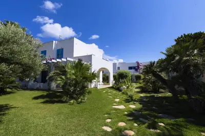 a white house with palm trees in a yard at Villa Turchese sul mare in San Vito lo Capo