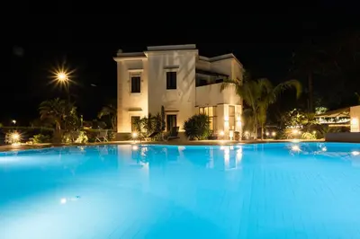 a large swimming pool in front of a house at night at Villa Masetta - Luxury Suites in Mondello