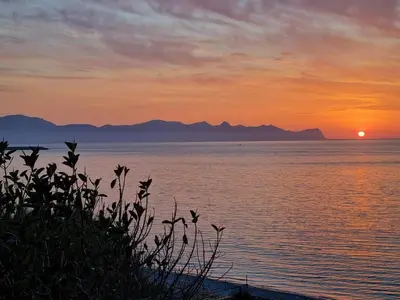 a sunset over the water with mountains in the background at LA FINESTRA SUL MARE in Trappeto