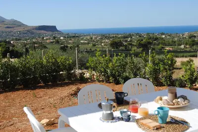 a white table and chairs with a view of a vineyard at Villa Edori - Giardino degli Allori in Castellammare del Golfo