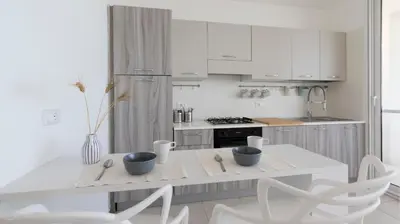 a white kitchen with a table and white chairs at Visitsicilia Azzurra Mare in Alcamo Marina