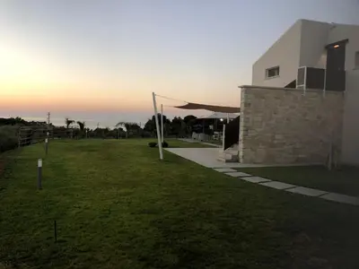a grassy yard next to a building with the sunset at Villa NATURE ZAGARA SCOPELLO ZINGARO in Castellammare del Golfo