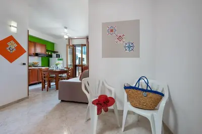 a living room with two white chairs and a kitchen at I Tre Golfi Beach Apartments in San Vito lo Capo