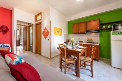 a living room with a table and a kitchen with green walls at I Tre Golfi Beach Apartments in San Vito lo Capo