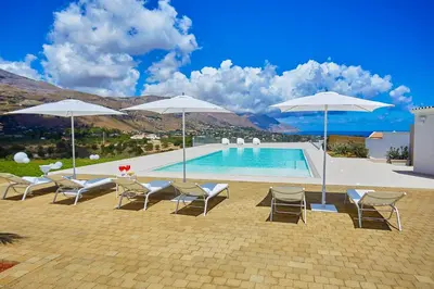 a swimming pool with chairs and umbrellas at Villa Etesiae in Castellammare del Golfo