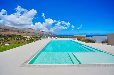 a swimming pool with two white chairs and a blue at Villa Etesiae in Castellammare del Golfo