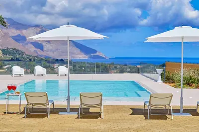 a pool with two chairs and a table and two umbrellas at Villa Etesiae in Castellammare del Golfo