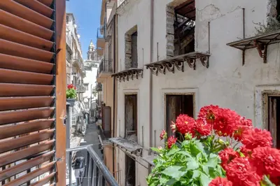 an alley with red flowers on a balcony at GuestHost - Vucciria Market Apartment with Balconies in Palermo