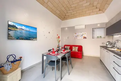 a kitchen and living room with a table and a red couch at Alofara Apartment in San Vito lo Capo