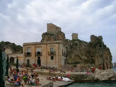 a group of people sitting on a beach in front of a building at La Perla del Golfo in Castellammare del Golfo