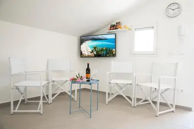 a room with white chairs and a table with a bottle of wine at Appartamenti in Villa Nature con vista mare e monti in Scopello