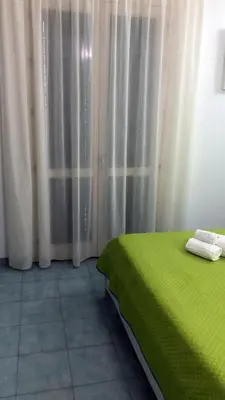 a bedroom with a green bed and white curtains at Le Camere della Campana in Castellammare del Golfo