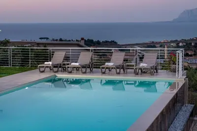 a swimming pool with chairs and the ocean in the background at Villa Maria con piscina e vista mare in Castellammare del Golfo