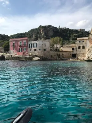 a boat in the water in front of houses at Casa Bouganville in Scopello