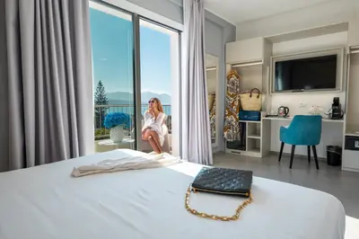 a woman sitting on a bed in a room with a large window at Resort La Battigia Beach & Spa in Alcamo Marina