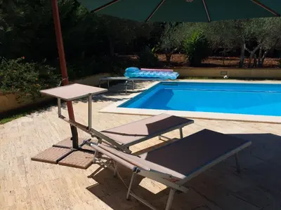 an umbrella and two chairs next to a swimming pool at Villa Flora in Castellammare del Golfo