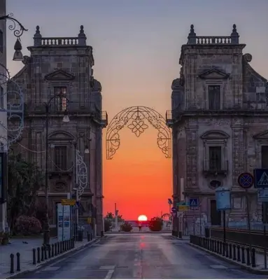 two buildings on a street with a sunset in the background at Cathedral House Design in Palermo