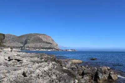 a rocky shoreline with a mountain in the background at Casa de Paoli - Vista Mare Arenella, Palermo con Parcheggio Privato in Palermo
