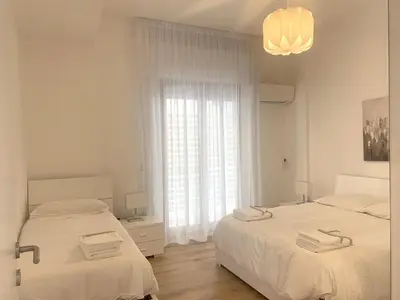 a white bedroom with two beds and a window at Residence D'azeglio in Palermo