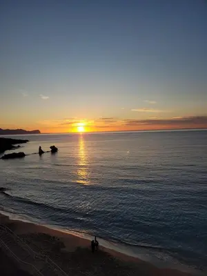 a sunset over the ocean with people walking on the beach at JEY STUDIO_INDEPENDENT SEAFRONT APARTMENT in Terrasini
