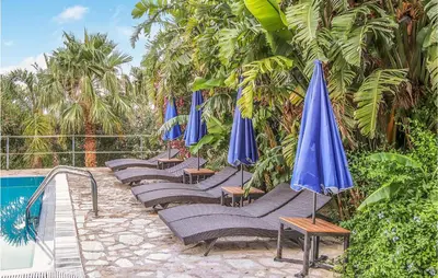 a row of lounge chairs with blue umbrellas next to a pool at Pietro 4 in San Vito lo Capo