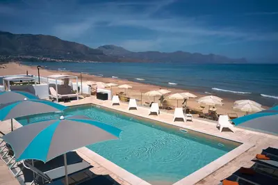 a swimming pool next to a beach with umbrellas at Hotel La Battigia in Alcamo Marina
