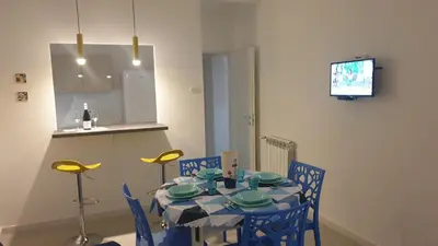 a dining room table with blue chairs and a television at Mami Holiday House in Castellammare del Golfo