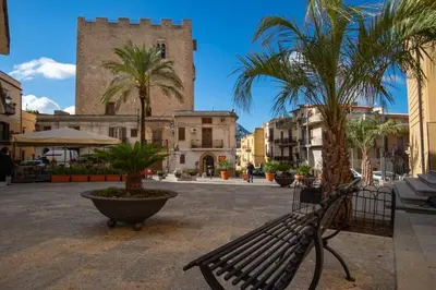 a bench in a square with palm trees and a tower at Casa di Lia in Montelepre