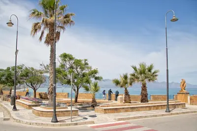 a park with palm trees and a statue next to the ocean at Alta Marea Sea Apartments in Balestrate