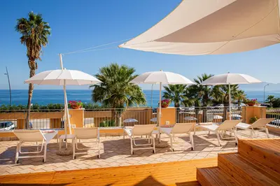 a patio with chairs and umbrellas and the ocean at Hotel Punta Nord Est in Castellammare del Golfo