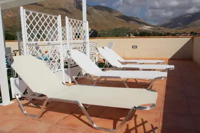 four white chairs on a balcony with mountains in the background at Catarin Comfort Rooms in Castelluzzo