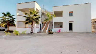 a large white building with palm trees and chairs at Case Playa in Balestrate