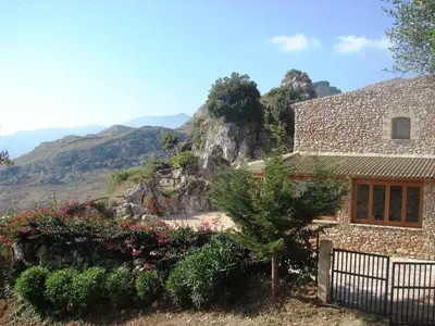 a house in the mountains with flowers in front of it at Casale Corcella in Scopello