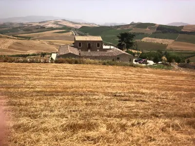 a field of dry grass with a building in the background at Masseria Baglio Perciata in Camporeale